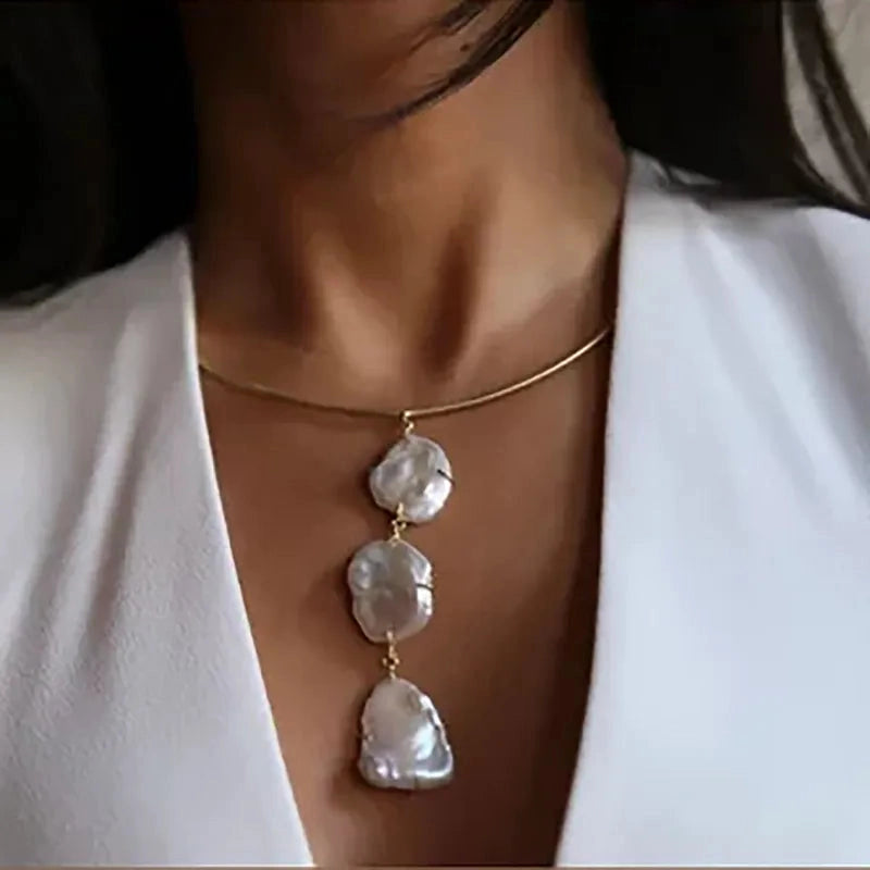 Model wearing a structured Aura 18K gold plated tubular collar necklace with a vertical drop of three large organic freshwater pearls.