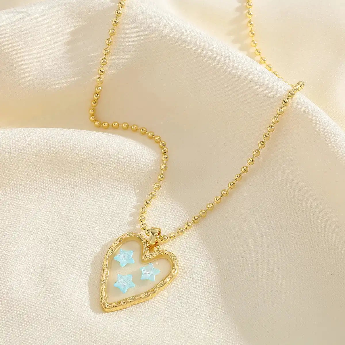 Close-up of Corazon Azul 18K gold plated necklace with blue star heart pendant on a soft cream fabric background