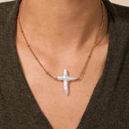 Model wearing the Celestial Pearl Cross Necklace featuring an organic white Baroque pearl pendant on a gold titanium steel chain.