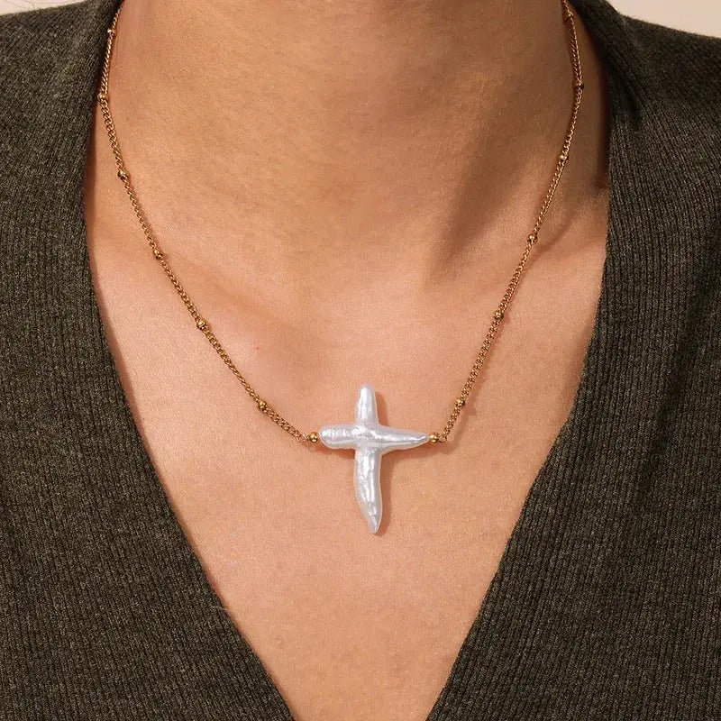 Model wearing the Celestial Pearl Cross Necklace featuring an organic white Baroque pearl pendant on a gold titanium steel chain.