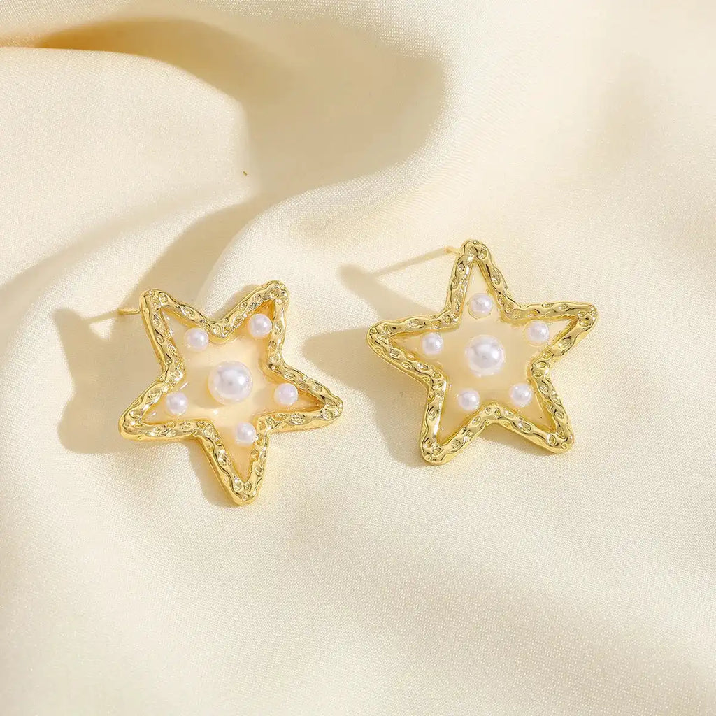 Waterproof Gold Perla Estrella Star Earrings in 18K gold plated stainless steel on a beige fabric background