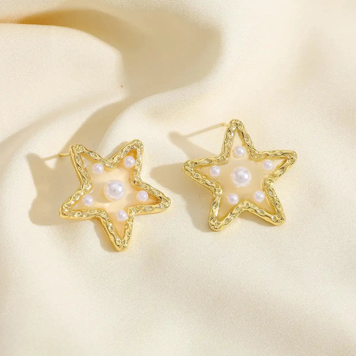 Waterproof Gold Perla Estrella Star Earrings in 18K gold plated stainless steel on a beige fabric background