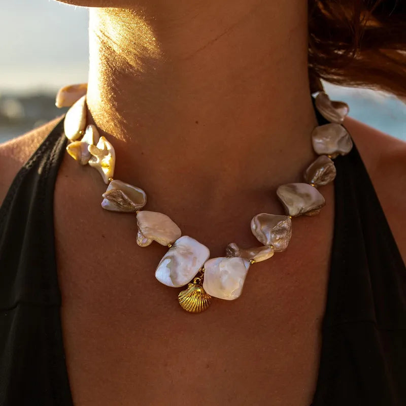 Waterproof Gold Shell Charm Pendant Necklace in 18K gold plated stainless steel worn by a person outdoors. | 7th of April